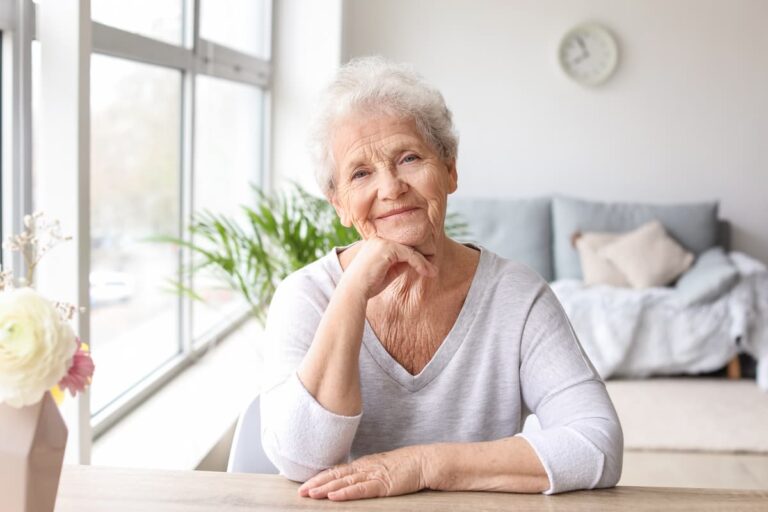 Novellus Clairemont | Senior woman smiling in apartment sitting at a table